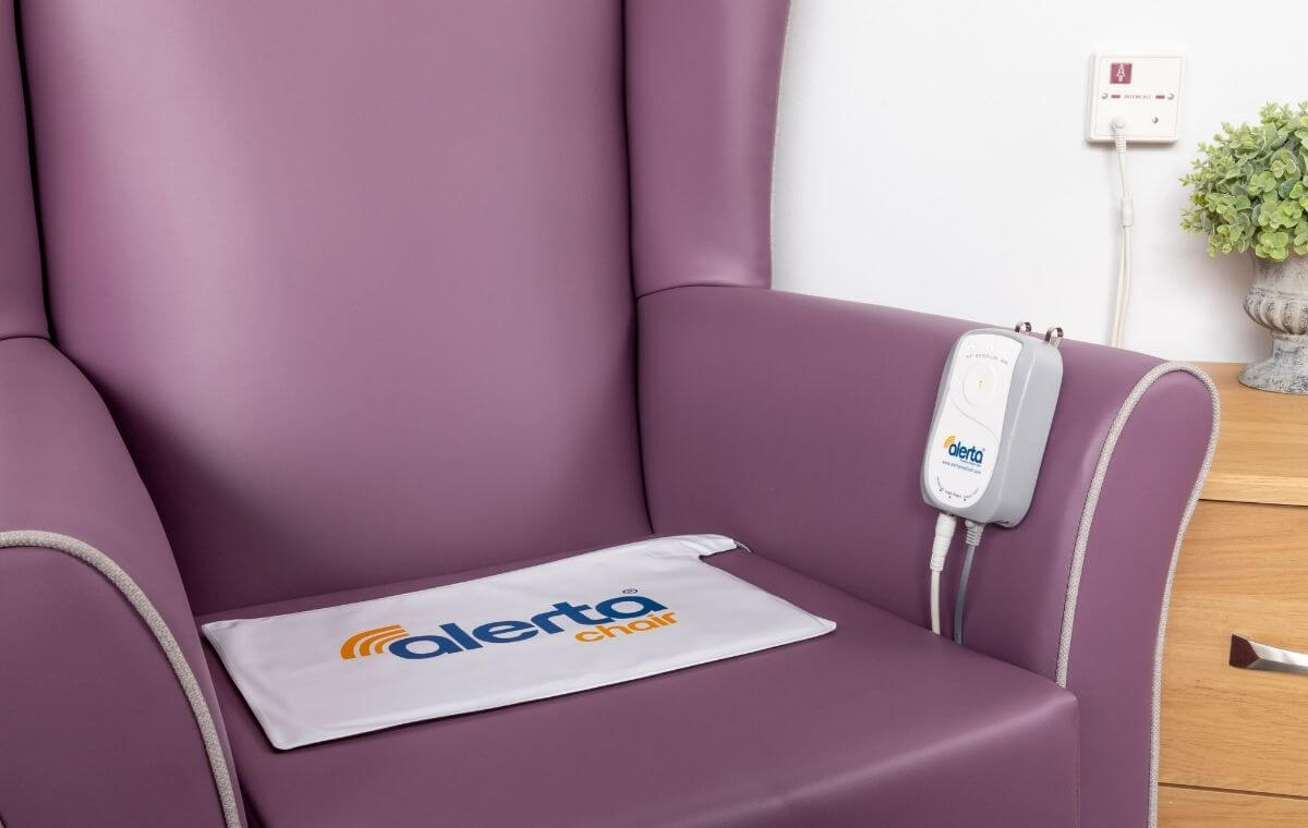 The image shows a fall alarm system called Alertamat, which includes a white pad with a blue and yellow logo, a bed pad, an alarm monitor and cables from Adaptive Equipment (Image 2).