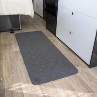 A rectangular, gray anti-slip floor mat placed on a wooden floor, near a white vehicle's entrance - Adaptive Equipment (Image 1).